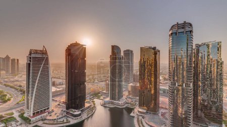 Foto de Salida del sol sobre altos edificios residenciales en la antena del distrito JLT, parte del distrito de uso mixto del centro de productos básicos de Dubai. Rascacielos alrededor del estanque - Imagen libre de derechos