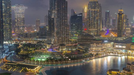 Foto de Rascacielos que se elevan por encima del centro de Dubái transición día a noche, centro comercial y fuente rodeada de edificios modernos vista aérea superior con cielo nublado colorido - Imagen libre de derechos