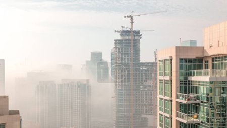 Photo for Dubai skyscrapers covered by morning fog in business bay district with construction site during sunrise . Aerial view from top of downtown in United Arab Emirates. - Royalty Free Image