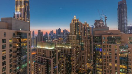 Téléchargez les photos : Les gratte-ciel de Dubaï avec un ciel doré sur la baie d'affaires transition jour-nuit. Vue aérienne du centre-ville des Émirats arabes unis. - en image libre de droit