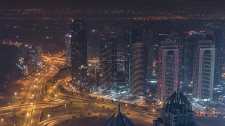 Foto de Rascacielos deportivos JLT y Dubai cerca de Sheikh Zayed Road durante toda la noche aérea. Edificios residenciales y tráfico en la intersección de carreteras. Luces agotándose - Imagen libre de derechos