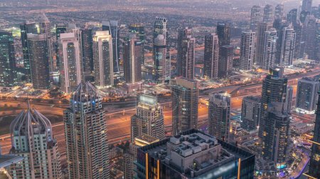 Foto de Rascacielos JLT y Dubai marina cerca de Sheikh Zayed Road día a noche transición aérea. Edificios residenciales iluminados y tráfico por carretera - Imagen libre de derechos