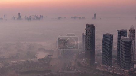 Photo for Big crossroad junction between JLT district and Dubai Marina intersected by Sheikh Zayed Road night to day transition aerial . Cars traffic covered by morning fog - Royalty Free Image