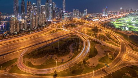 Téléchargez les photos : Panorama of Dubai Marina highway intersection spaghetti junction day to night transition . Illuminated tallest skyscrapers after sunset and golf club on a background. Aerial top view from JLT district - en image libre de droit