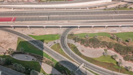 Photo for Aerial view on a big highway intersection  in Dubai Marina with shadows moving fast around, UAE. Cars traffic view from JLT district. Green lawn and trees with palms - Royalty Free Image