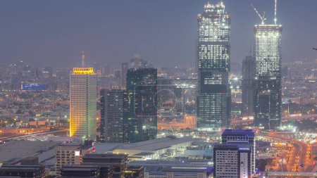 Téléchargez les photos : Vue aérienne des gratte-ciel avec World Trade Center à Dubaï transition jour-nuit après le coucher du soleil. Site de construction de nouvelles tours jumelles. Bur Dubai et le district de Deira sur un fond - en image libre de droit