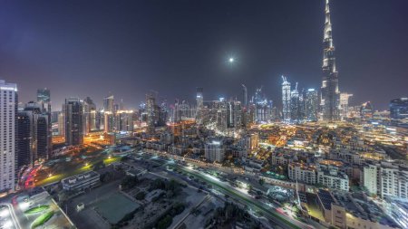 Téléchargez les photos : Dubaï Centre-ville pendant toute la nuit panorama avec le plus haut gratte-ciel et d'autres tours éclairées vue du sommet à Dubaï, Émirats arabes unis. Lune sur le ciel et lumières éteintes - en image libre de droit