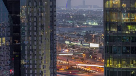 Téléchargez les photos : Villas et hôtel célèbre dans la ligne d'horizon du centre-ville de Dubaï avec une grande intersection aérienne de jour à la transition de nuit. Encadré par des gratte-ciel avec des fenêtres éclatantes - en image libre de droit
