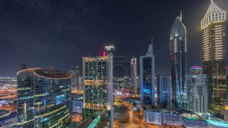 Foto de Dubai centro financiero internacional rascacielos panorámica noche aérea. Vista de torres iluminadas desde arriba con estacionamiento y tráfico en una carretera - Imagen libre de derechos