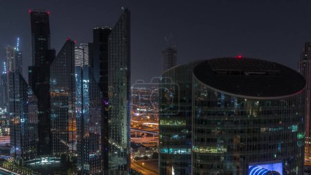 Téléchargez les photos : Dubai centre financier international gratte-ciel aérien toute la nuit. Vue des tours éclairées d'en haut avec des lumières éteintes. Trafic à l'intersection - en image libre de droit