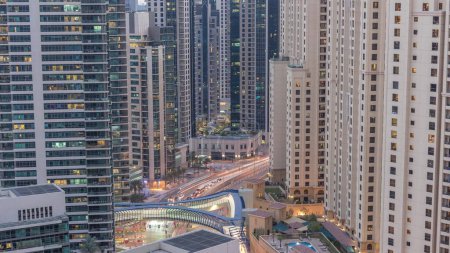 Téléchargez les photos : Vue d'ensemble de JBR et Dubai Marina skyline avec gratte-ciel modernes gratte-ciel front de mer vivant appartements aérien jour à nuit transition. Trafic routier à l'intersection et passerelle - en image libre de droit