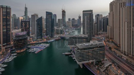 Foto de Aerial view to Dubai marina skyscrapers and jbr towers around canal with floating boats day to night transition . White boats are parked in yacht club after sunset - Imagen libre de derechos