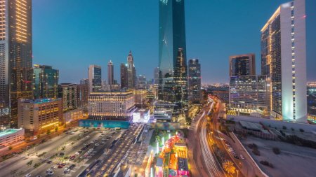 Téléchargez les photos : Dubai International Quartier financier transition jour-nuit. Vue aérienne panoramique du parking et des tours de bureaux d'affaires après le coucher du soleil. gratte-ciel avec hôtels et centres commerciaux près du centre-ville - en image libre de droit