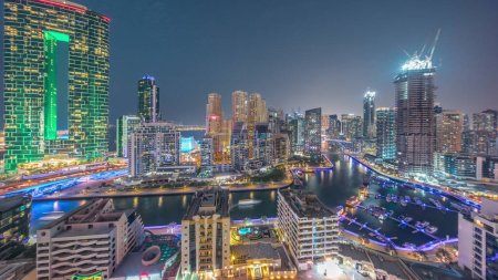 Photo for Panorama of Dubai Marina with several boat and yachts parked in harbor and skyscrapers around canal aerial day to night transition . Towers of JBR district on a background - Royalty Free Image