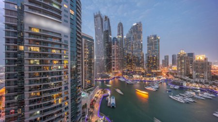 Photo for Dubai marina tallest skyscrapers with glowing windows and yachts in harbor aerial night after sunset. View at apartment buildings, hotels and office blocks, modern residential development of UAE - Royalty Free Image