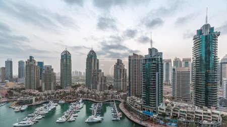 Téléchargez les photos : Luxury yacht bay in the city aerial night to day transition  in Dubai marina before sunrise. Modern skyscrapers along waterfront promenade and boats floating in harbor - en image libre de droit