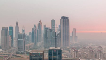 Foto de Panorama of Dubai Financial Center district with tall skyscrapers with illumination night to day transition . Aerial view to towers with morning fog before sunrise - Imagen libre de derechos