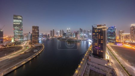 Téléchargez les photos : Paysage urbain de gratte-ciel dans la baie d'affaires de Dubaï avec canal d'eau panoramique de transition de jour à nuit. Skyline moderne avec tours et front de mer après le coucher du soleil. Un centre d'affaires international - en image libre de droit