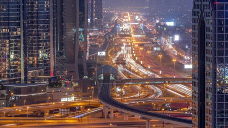 Téléchargez les photos : Occupé Sheikh Zayed Road transition aérienne de jour à la nuit, métro et gratte-ciel modernes autour dans la ville de Dubaï de luxe. Trafic lourd sur une autoroute avec de nombreuses voitures. Émirats arabes unis - en image libre de droit