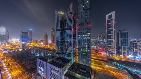 Photo for Aerial panorama of Dubai International Financial District with many skyscrapers during all night . Traffic on a road junction and Sheikh Zayed road with lights turning off. Dubai, UAE. - Royalty Free Image