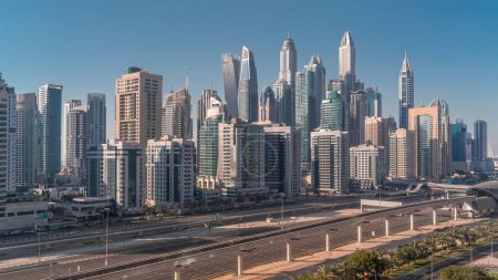 Téléchargez les photos : Dubai Marina plus haut bloc de gratte-ciel avec des ombres se déplaçant rapidement pendant toute la journée. Vue aérienne du quartier JLT vers les immeubles à appartements, les hôtels et les tours de bureaux près de l'autoroute jusqu'au coucher du soleil - en image libre de droit