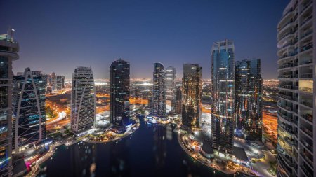Téléchargez les photos : Grands bâtiments résidentiels du quartier JLT transition aérienne du jour à la nuit, faisant partie du quartier mixte du centre multi-commodités de Dubaï. Vue panoramique sur les tours et les gratte-ciel - en image libre de droit