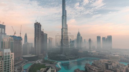 Téléchargez les photos : Vue aérienne de la ville de Dubaï tôt le matin pendant la nuit de brouillard au timelapse de transition de jour. Skyline panoramique futuriste de la ville avec des gratte-ciels et des tours d'en haut - en image libre de droit
