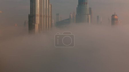 Téléchargez les photos : Vue aérienne de la ville de Dubaï tôt le matin pendant le temps de brouillard. Lever de soleil à horizon futuriste de la ville avec des gratte-ciel et des tours d'en haut. Soleil réfléchi par la surface du verre - en image libre de droit