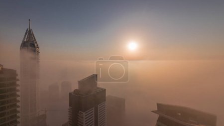 Photo for Sunrise over rare early morning winter fog above the Dubai Marina skyline and skyscrapers rooftops aerial timelapse. Top view from above clouds. Dubai, UAE - Royalty Free Image