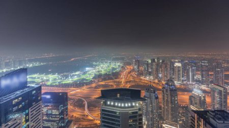Téléchargez les photos : Panorama de Dubai Marina avec gratte-ciel JLT et parcours de golf timelapse nocturne, Dubaï, Émirats arabes unis. Vue aérienne depuis les tours supérieures. Éclairage des lumières de ville - en image libre de droit