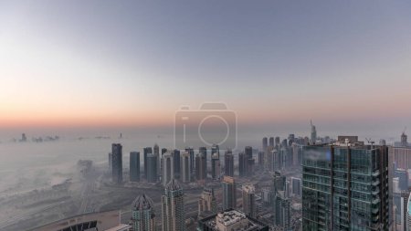 Téléchargez les photos : Panorama de Dubai Marina avec gratte-ciel JLT et parcours de golf nuit à jour timelapse transition, Dubaï, Émirats arabes unis. Vue aérienne depuis les tours matin brumeux. Skyline de la ville avec des toits - en image libre de droit
