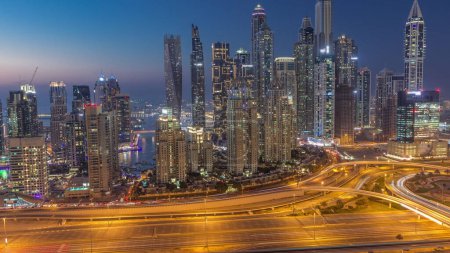 Photo for Skyscrapers of Dubai Marina with illuminated highest residential buildings day to night transition timelapse after sunset with traffic on a highway. Aerial top view from JLT district - Royalty Free Image