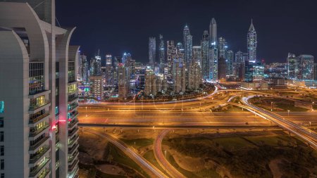 Photo for Panorama of Dubai Marina showing highway intersection spaghetti junction night timelapse. Illuminated tallest skyscrapers on a background. Aerial top view from JLT district. - Royalty Free Image