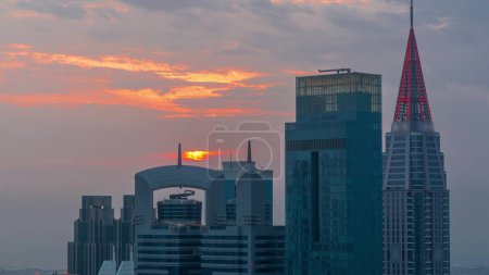 Foto de Puesta de sol sobre el centro financiero de la ciudad de Dubai con rascacielos de lujo timelapse, Dubai, Emiratos Árabes Unidos. Vista aérea con cielo anaranjado y tejados de torres con agujas - Imagen libre de derechos