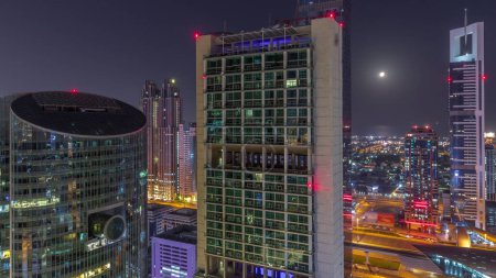 Photo for Dubai international financial center skyscrapers aerial during all night timelapse. Illuminated towers with lights turning off view from above. Moon setting down - Royalty Free Image
