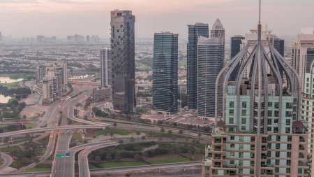 Téléchargez les photos : Énorme carrefour routier entre le quartier JLT et Dubai Marina recoupé par Cheikh Zayed Road timelapse matin aérien. Terrain de golf près des tours éclairées et des gratte-ciel avec un trafic achalandé - en image libre de droit