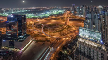 Téléchargez les photos : Panorama montrant la marina de Dubaï et les gratte-ciel illuminés par JLT le long de Sheikh Zayed Road avec une énorme jonction et un quartier médiatique nocturne aérien. Immeubles résidentiels et de bureaux d'en haut. - en image libre de droit