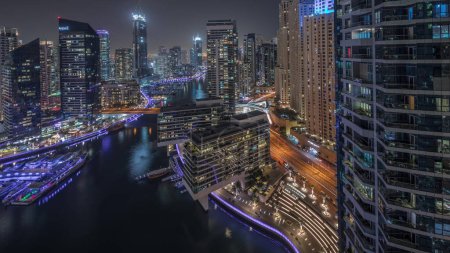 Téléchargez les photos : Panorama montrant vue aérienne sur la marina de Dubaï illuminé gratte-ciel autour du canal avec yachts flottants timelapse de nuit. Tours dans les districts jlt et jbr. Les bateaux blancs sont garés dans le yacht club - en image libre de droit