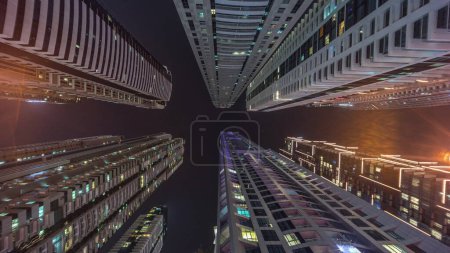 Foto de Mira hacia el cielo nocturno con rascacielos más altos con ventanas iluminadas. Amplia perspectiva de ángulo de la selva urbana en Dubai marina - Imagen libre de derechos