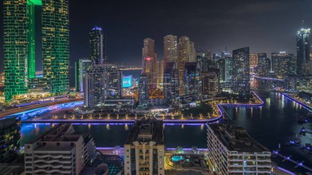 Photo for Panorama showing Dubai Marina skyscrapers and JBR district with luxury buildings and resorts aerial night timelapse. Illuminated waterfront and boats floating in canal - Royalty Free Image