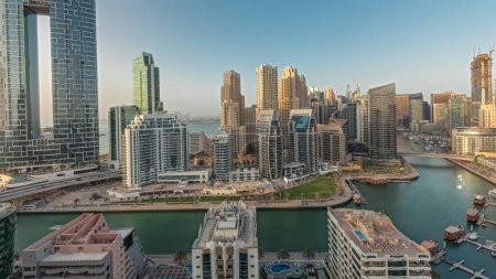 Téléchargez les photos : Panorama montrant les gratte-ciel de Dubai Marina et le quartier JBR avec des bâtiments de luxe et des stations aériennes timelapse. Bord de l'eau avec palmiers et bateaux flottant dans le canal - en image libre de droit