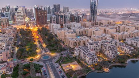 Téléchargez les photos : Bâtiments de faible hauteur dans le quartier des Verts et gratte-ciel dans le quartier de Barsha Heights transition aérienne du jour à la nuit timelapse panoramique. Skyline de Dubaï avec palmiers et arbres - en image libre de droit