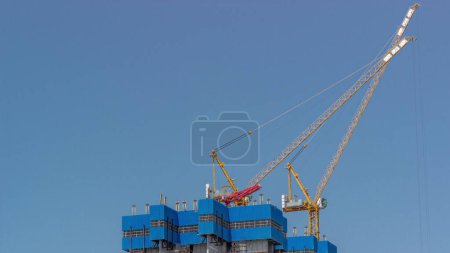Photo for Cranes working on big constraction site works of new skyscraper timelapse against blue sky. Urban development of high-rise tower and building activity - Royalty Free Image