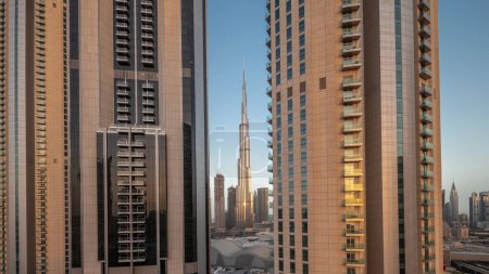 Téléchargez les photos : Les plus hauts gratte-ciel du centre-ville de Dubai situé sur la rue bouleward près du centre commercial aérien nuit à la transition de jour timelapse. Soleil réfléchi par la surface du verre au lever du soleil - en image libre de droit
