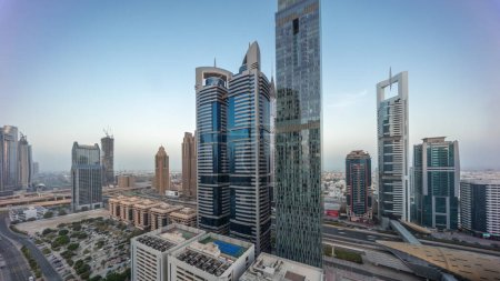 Téléchargez les photos : Vue aérienne panoramique du quartier financier international de Dubaï avec de nombreux gratte-ciel nuit à jour passage timelapse. Trafic sur un carrefour routier sur la route Cheikh Zayed avant le lever du soleil. Dubai, Émirats arabes unis. - en image libre de droit