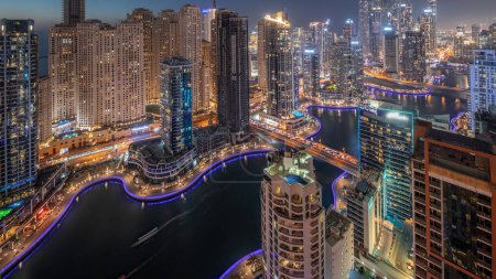Téléchargez les photos : Vue de différents gratte-ciel dans le plus haut bloc recidential de Dubai Marina et JBR district aérien jour à nuit timelapse transition avec canal artificiel. Nombreuses tours et yachts après le coucher du soleil - en image libre de droit