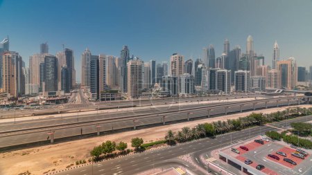 Téléchargez les photos : Panorama du port de plaisance de Dubaï plus haut bloc de gratte-ciel timelapse pendant toute la journée. Vue aérienne du quartier JLT vers les immeubles à appartements, les hôtels et les tours de bureaux près de l'autoroute avec des ombres se déplaçant rapidement - en image libre de droit