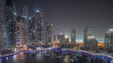 Téléchargez les photos : Panorama showing Dubai marina tallest skyscrapers and yachts in harbor aerial night . View at apartment buildings, hotels and office blocks, modern residential development of UAE - en image libre de droit