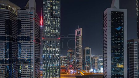 Téléchargez les photos : Panorama showing aerial view of Dubai International Financial District with many illuminated skyscrapers night . Traffic on a road near multi storey parkings. Dubai, UAE. - en image libre de droit