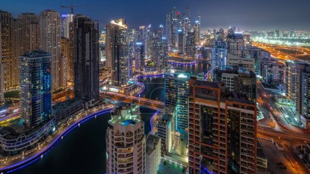 Téléchargez les photos : Vue de divers gratte-ciel dans le plus haut bloc recidential de Dubai Marina transition aérienne de jour à la nuit avec canal artificiel et des ponts au-dessus. Nombreuses tours et yachts après le coucher du soleil - en image libre de droit